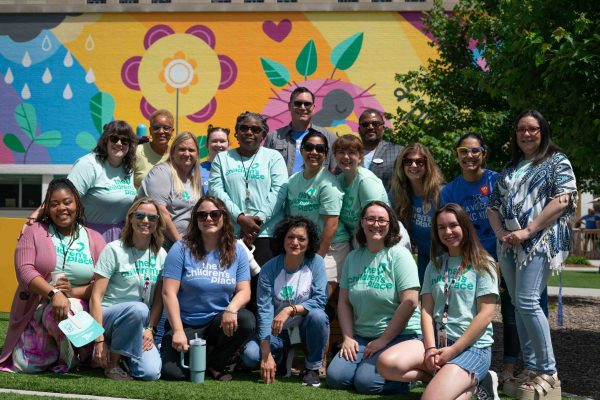 The Children's Place staff poses on the playground. Behind them is a large, colorful mural.